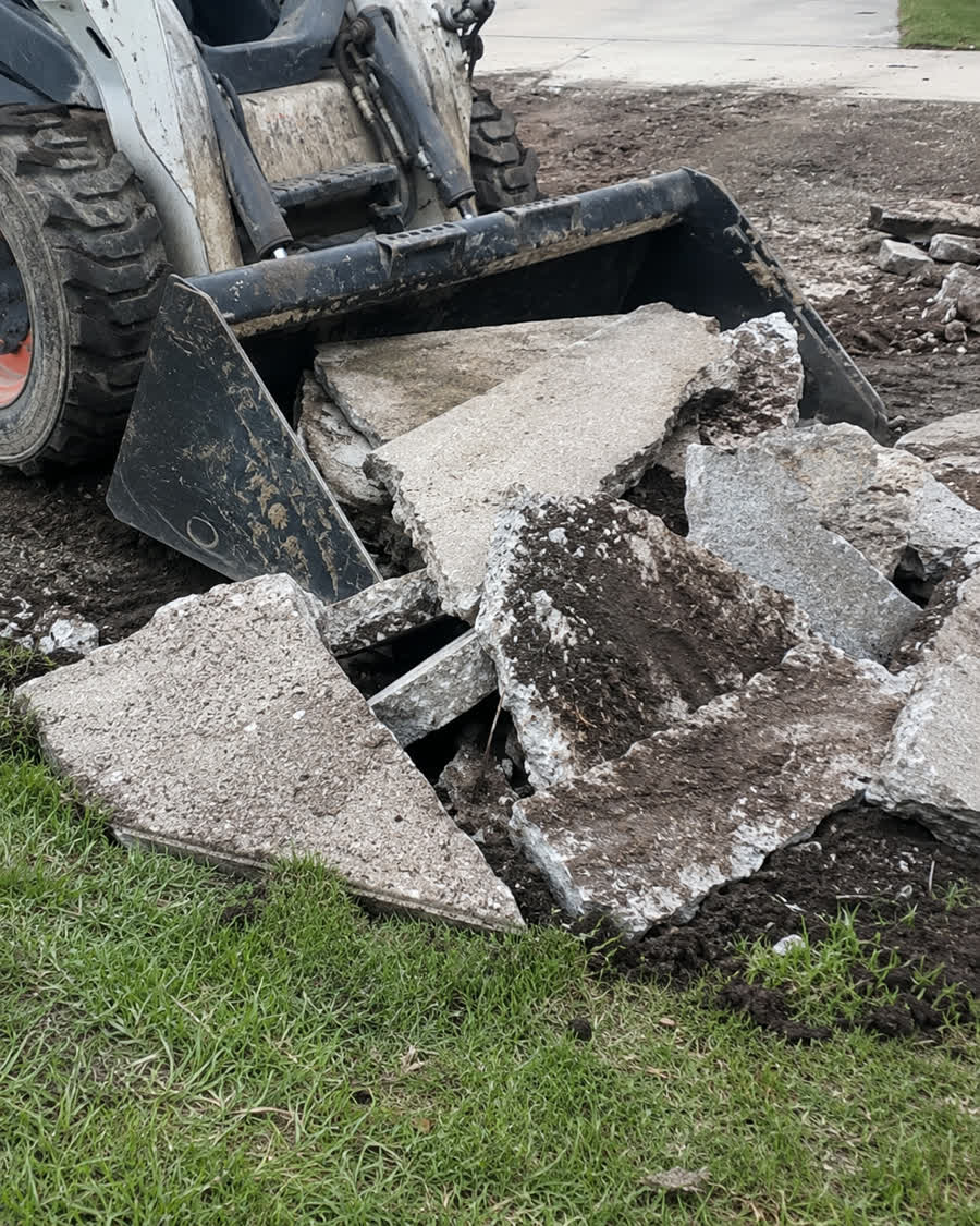 Compact loader gathering broken concrete at a residential removal site